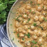 Creamy garlic mushrooms in a skillet next to a bunch of fresh herbs