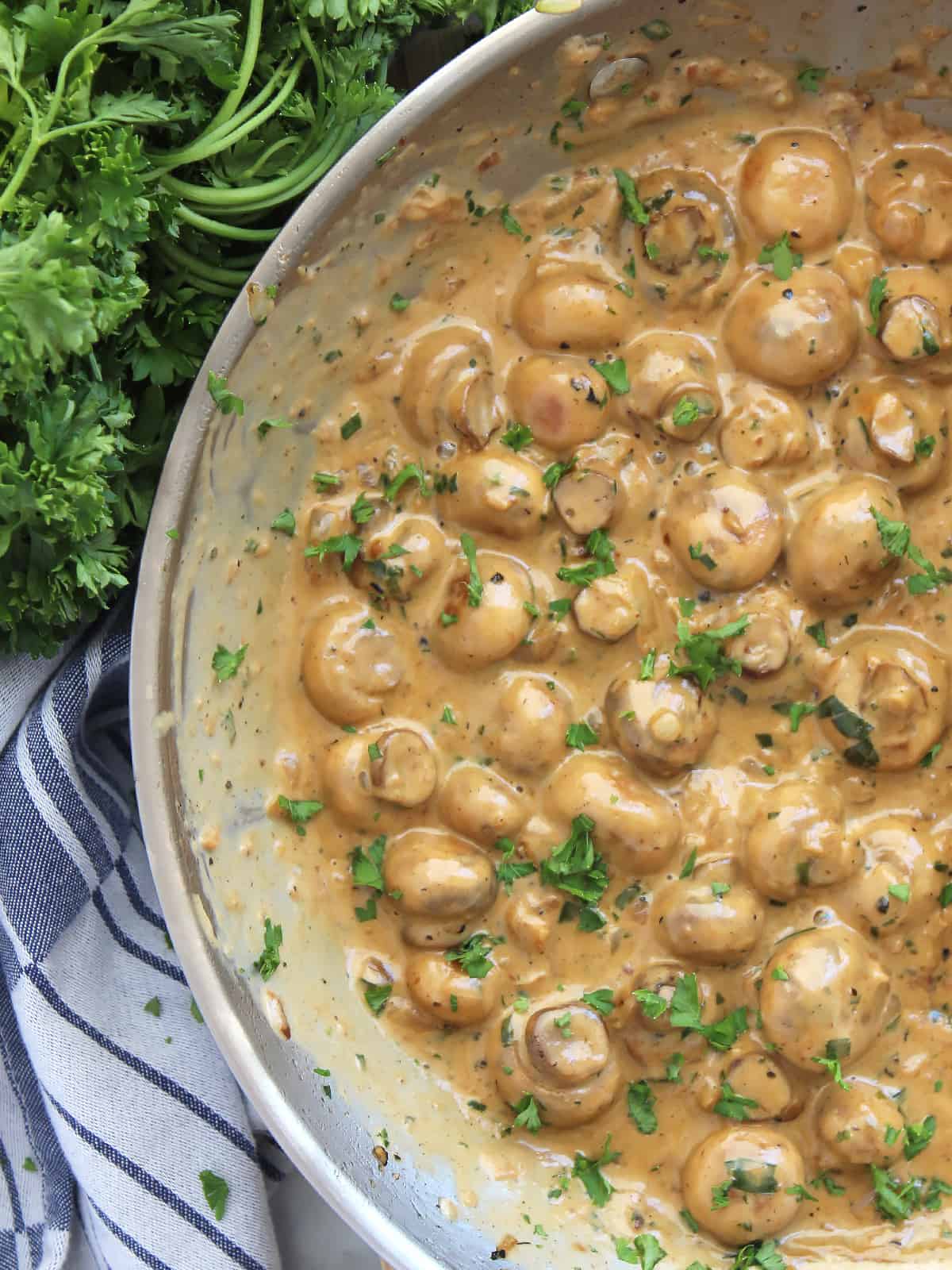 Creamy garlic mushrooms in a skillet next to a bunch of fresh herbs