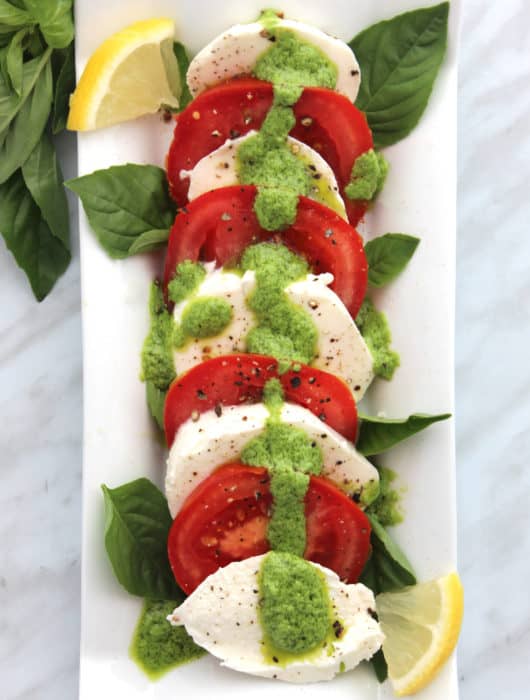 Overhead shot of pesto caprese salad on a white serving plate.