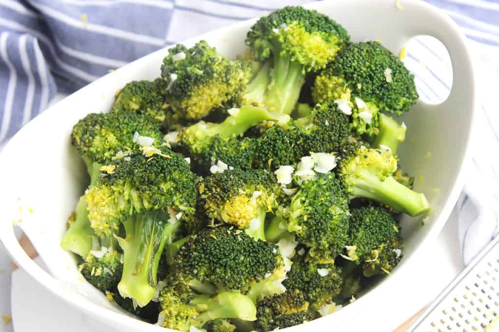 The cooked broccoli in a bowl topped with grated lemon zest.