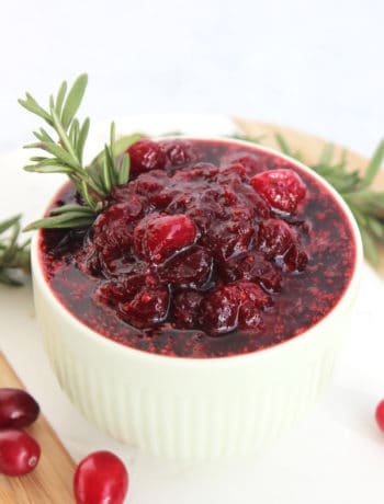 Cranberry brown sugar sauce in a small bowl next to fresh cranberries and rosemary.