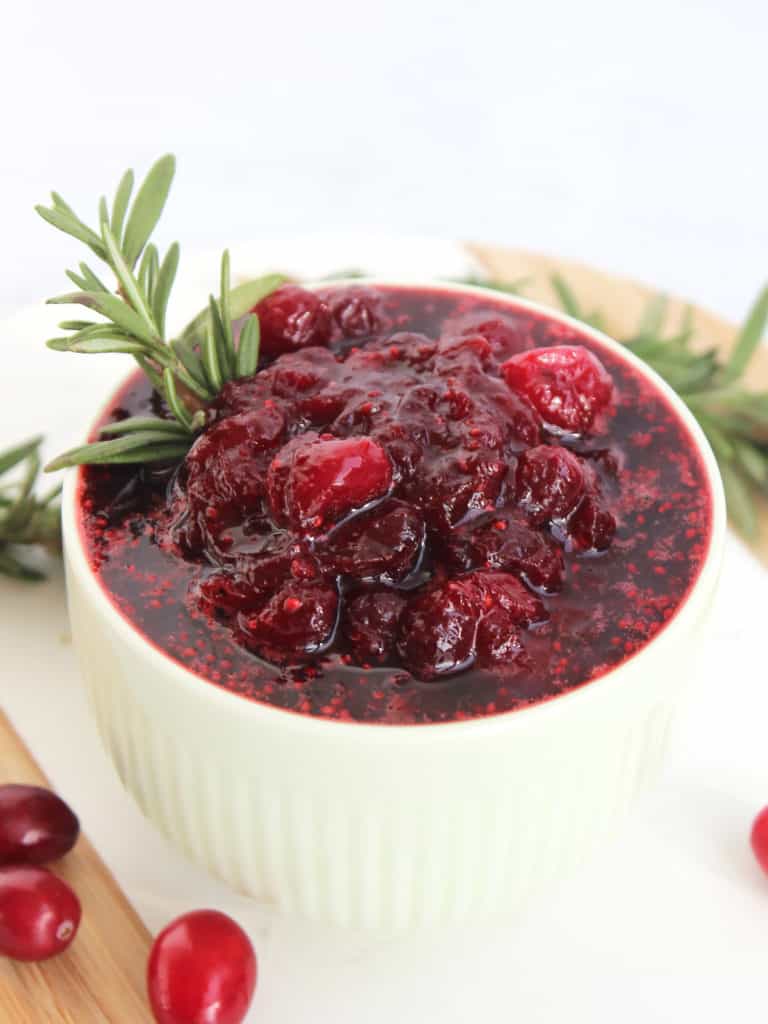 Cranberry brown sugar sauce in a small bowl next to fresh cranberries and rosemary.