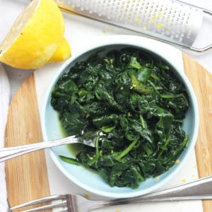 A fork in a bowl of buttered spinach on a wooden chopping board.