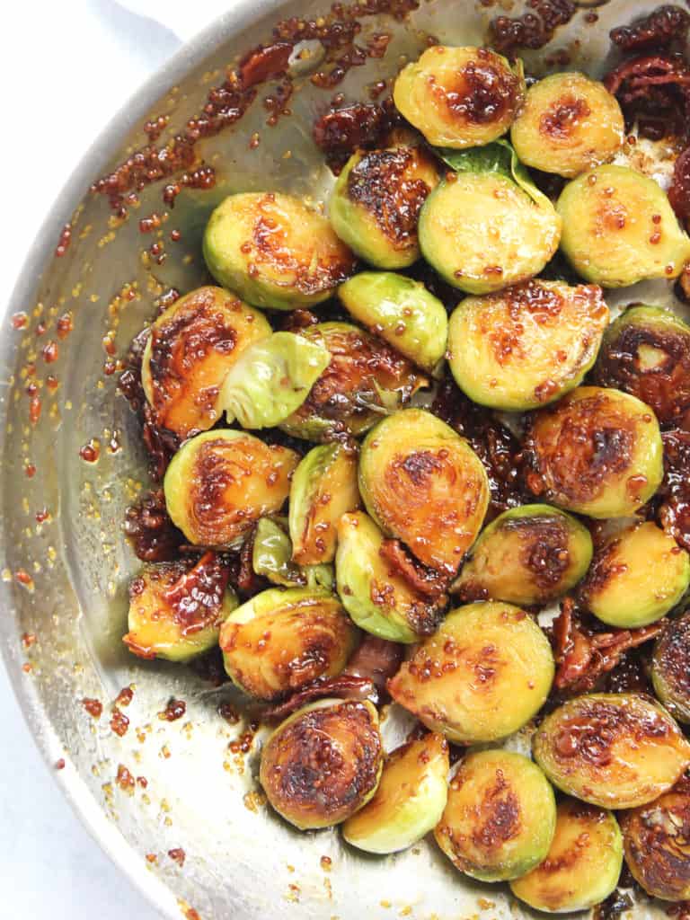 Close up of halved Brussel sprouts in a skillet in sauce.