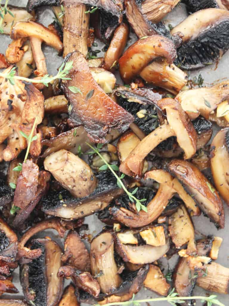 Close up of roasted mushrooms on a baking sheet with fresh thyme sprigs.