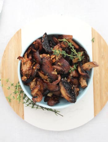 A bowl of roasted mushrooms on a white and wood chopping board.