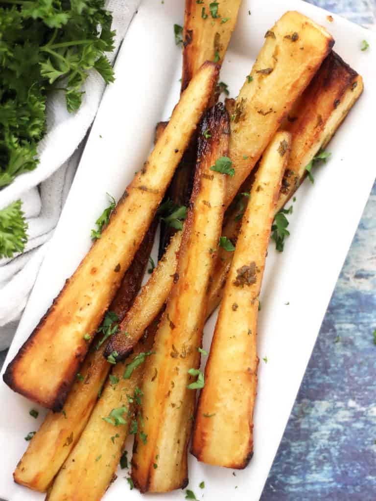 Honey mustard glazed parsnips on a white plate next to a bunch of parsley.