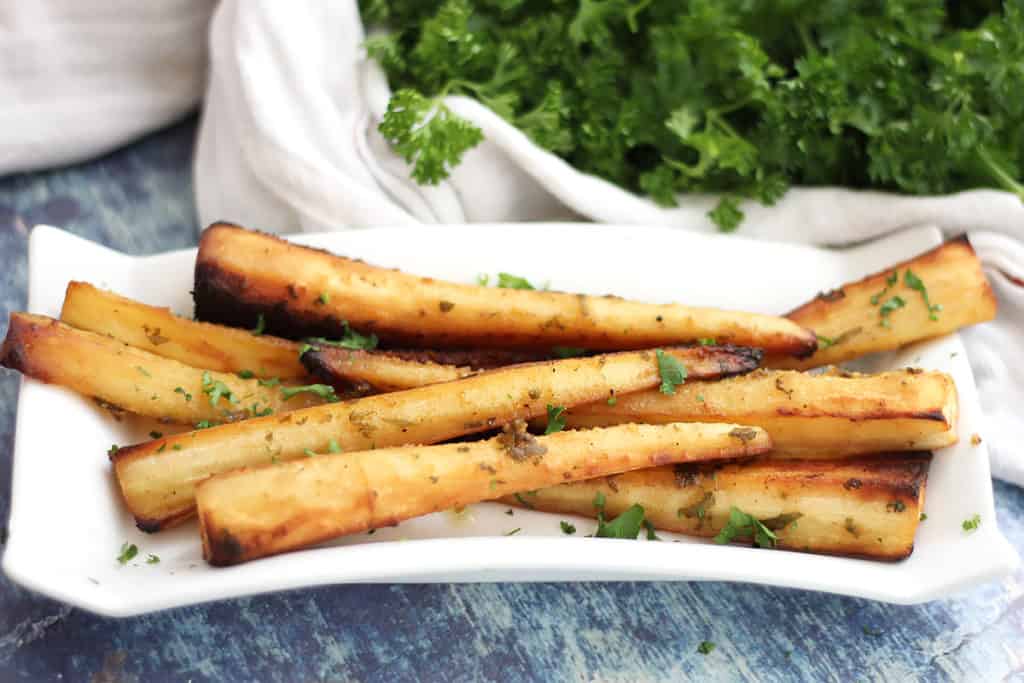 Honey mustard parsnips on a plate garnished with fresh parsley.