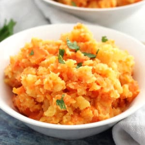Rutabaga carrot mash served in a white bowl and garnished with fresh parsley.