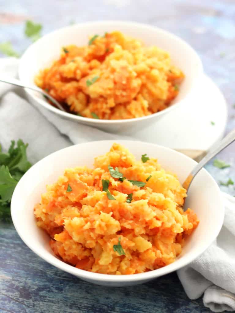 Rutabaga carrot mash served in two white bowls with spoons.