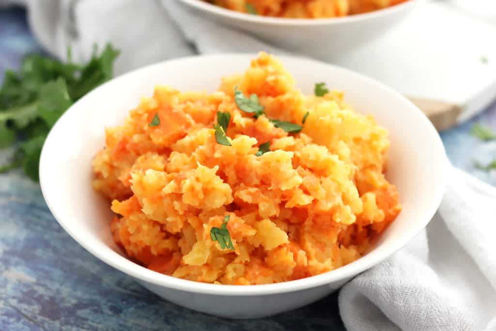 Rutabaga and carrot mash in a white bowl served with fresh herbs.