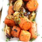 Close up over roasted carrots and Brussels garnished with fresh herbs.