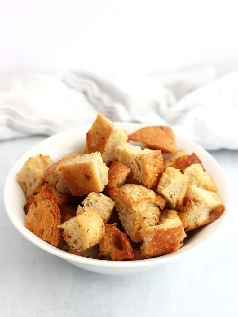 A bowl of garlic butter croutons in front of a white cloth.