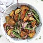 Roasted potato salad served in a large marble serving bowl with two spoons.