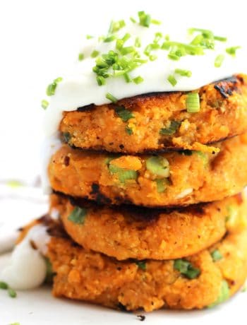 Four sweet potato cakes stacked on top of each other with sour cream and chopped chives.