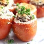 A stuffed tomato on a white plate garnished with fresh parsley.