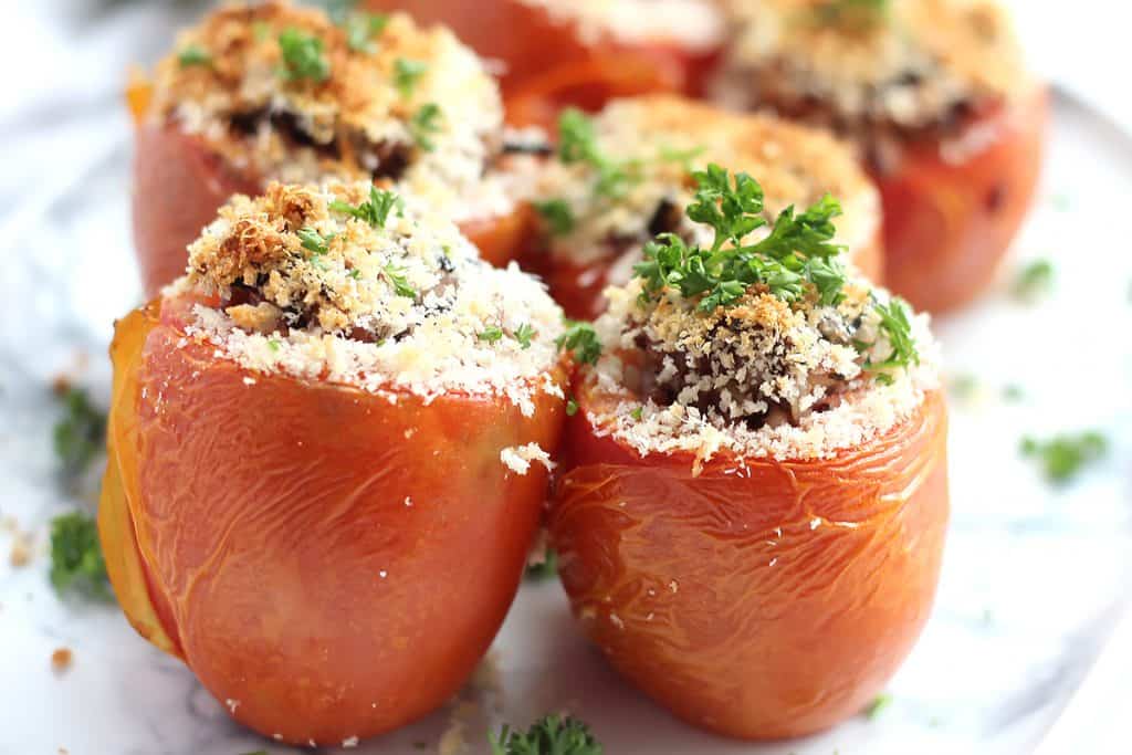 Side view of six rice stuffed tomatoes on a serving plate.