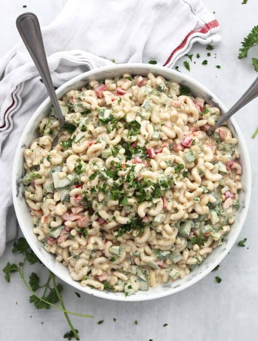 Cajun pasta salad in a serving bowl with two spoons and garnished with fresh herbs.