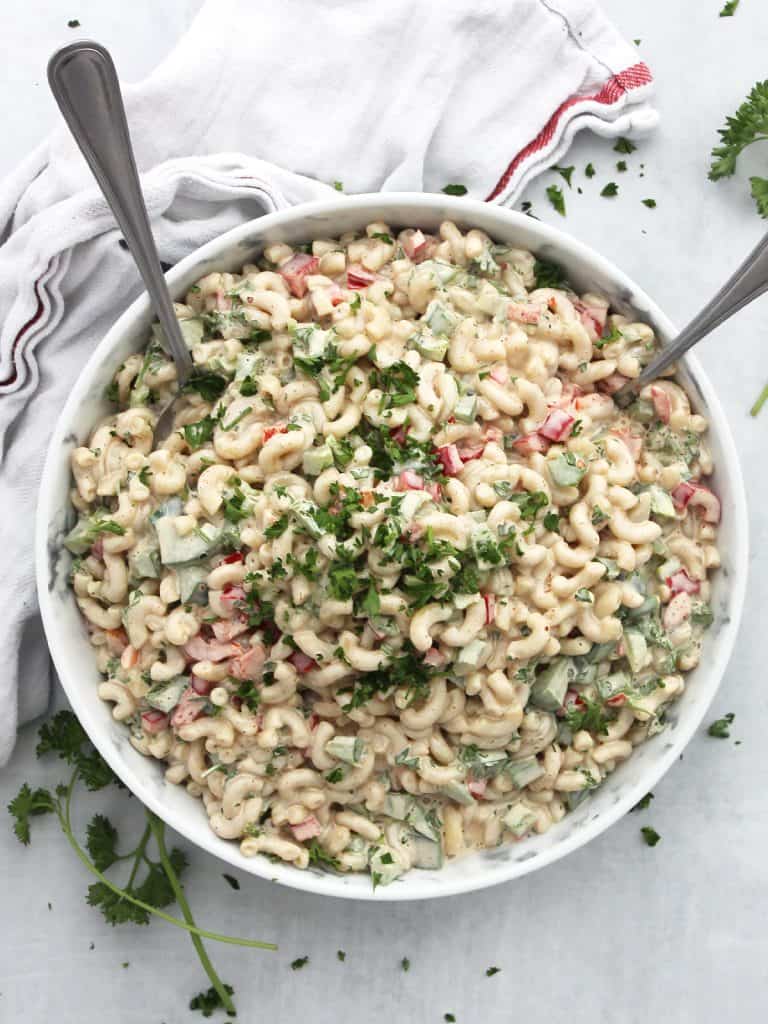 Cajun pasta salad in a serving bowl with two spoons and garnished with fresh herbs.