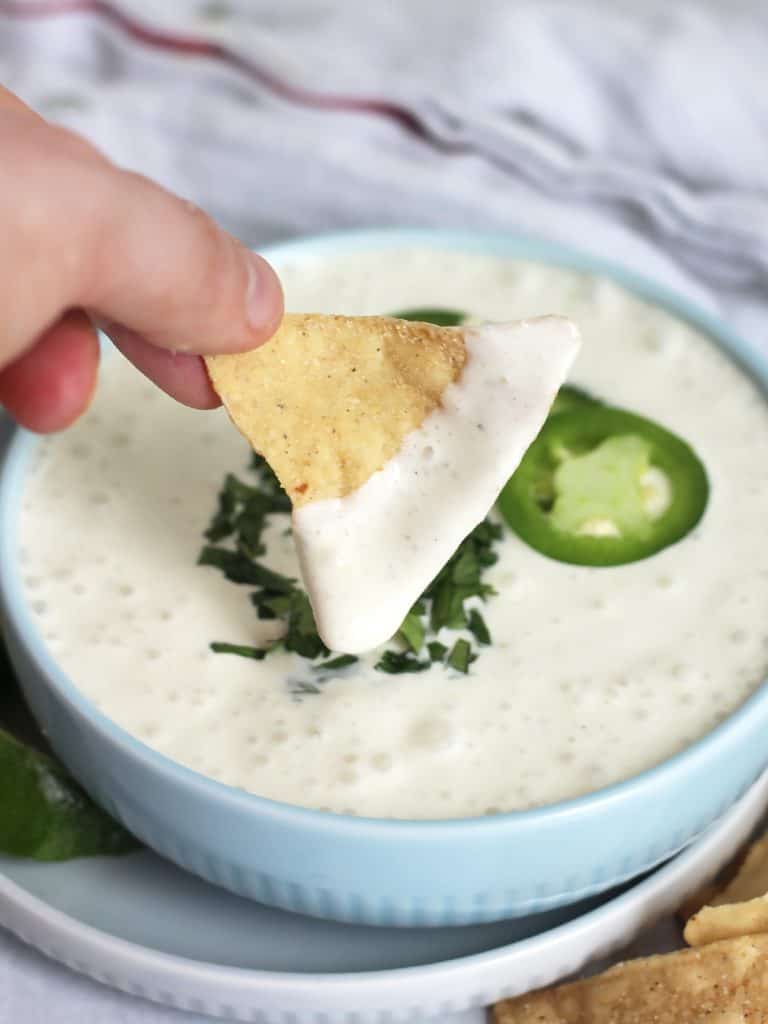 A tortilla chip being dipped into the jalapeno sour cream.