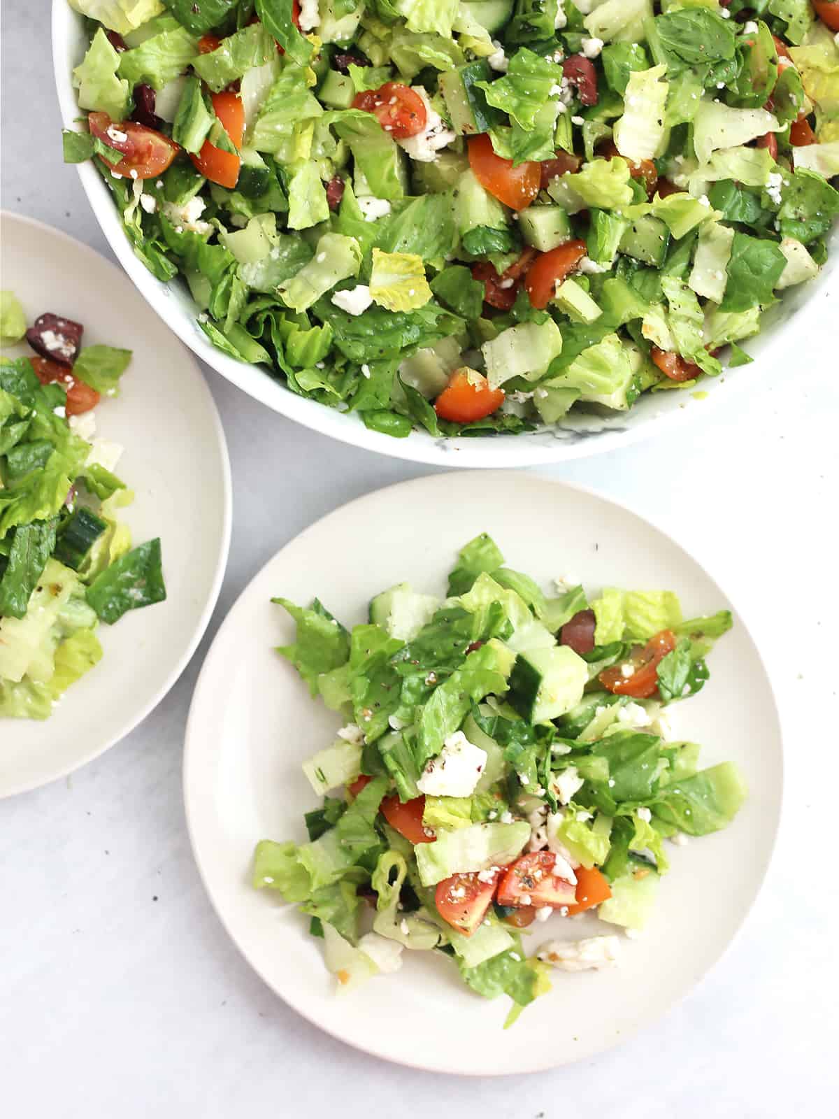 Greek lettuce sald in a large serving bowl and served on to two small side plates.