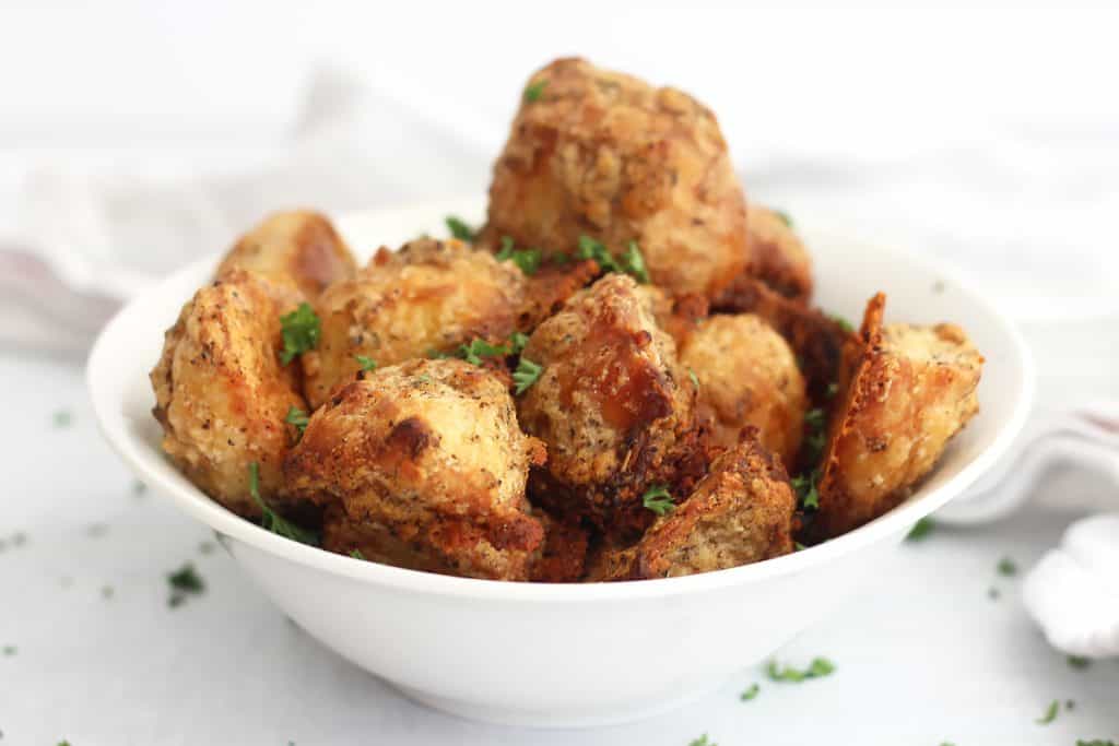 Parmesan crusted roasted potatoes in a white serving bowl.