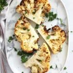 Two cauliflower steaks cut in half and served on a plate with a garnish of fresh parsley.