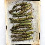 Roasted pesto asparagus on a parchment lined baking sheet.