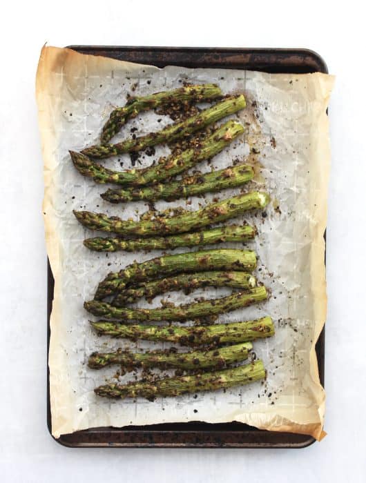 Roasted pesto asparagus on a parchment lined baking sheet.