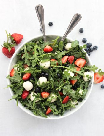 Red white and blue salad in a large serving bowl with two spoons.