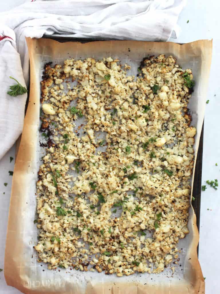 The cauliflower on a lined baking sheet garnished with fresh herbs after being roasted,