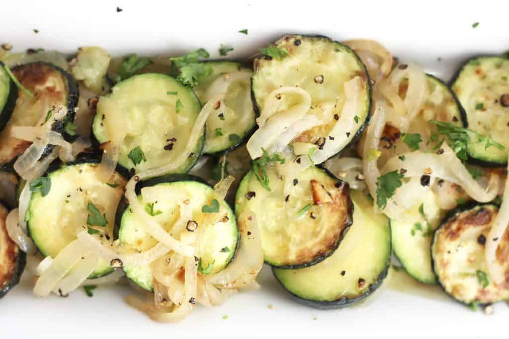 Overhead shot of sautéed zucchini and onions garnished with fresh herbs.