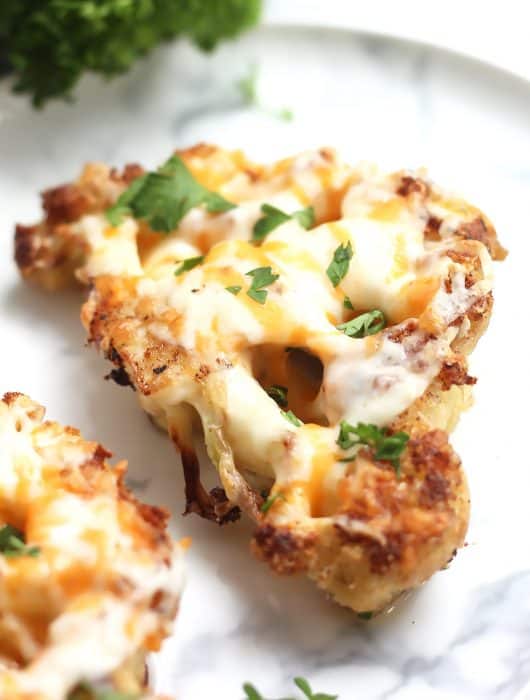 A cauliflower steak covered with melted cheese and garnished with fresh parsley.