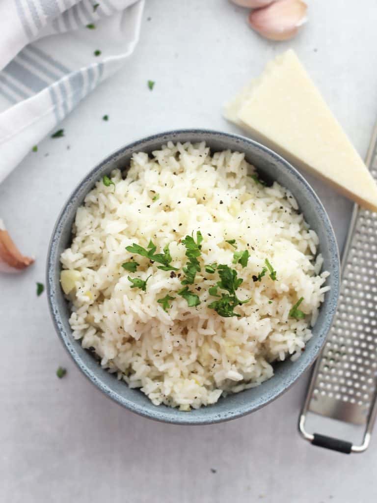 Overhead shot of a bowl of rice next to a wedge of parmesan and garlic cloves.
