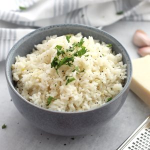 Garlic parmesan rice in a bowl topped with fresh herbs.