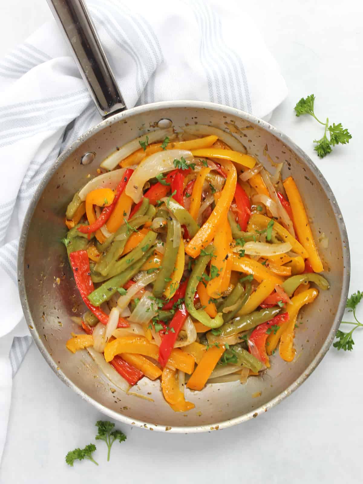 Overhead shot of sautéed bell peppers and onions in a skillet garnished with fresh herbs.