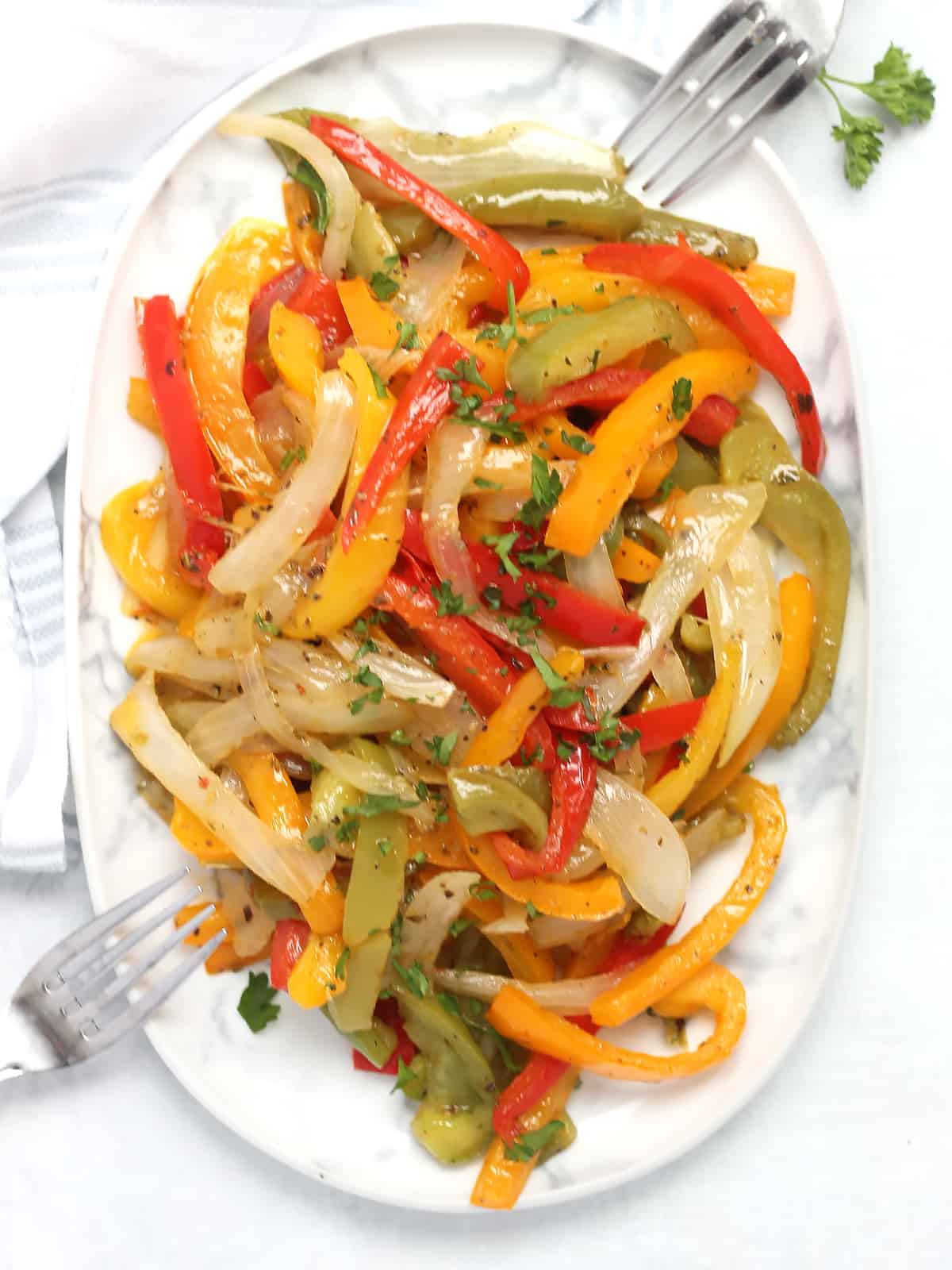 Overhead shot of sautéed peppers and onions on a plate with two forks.