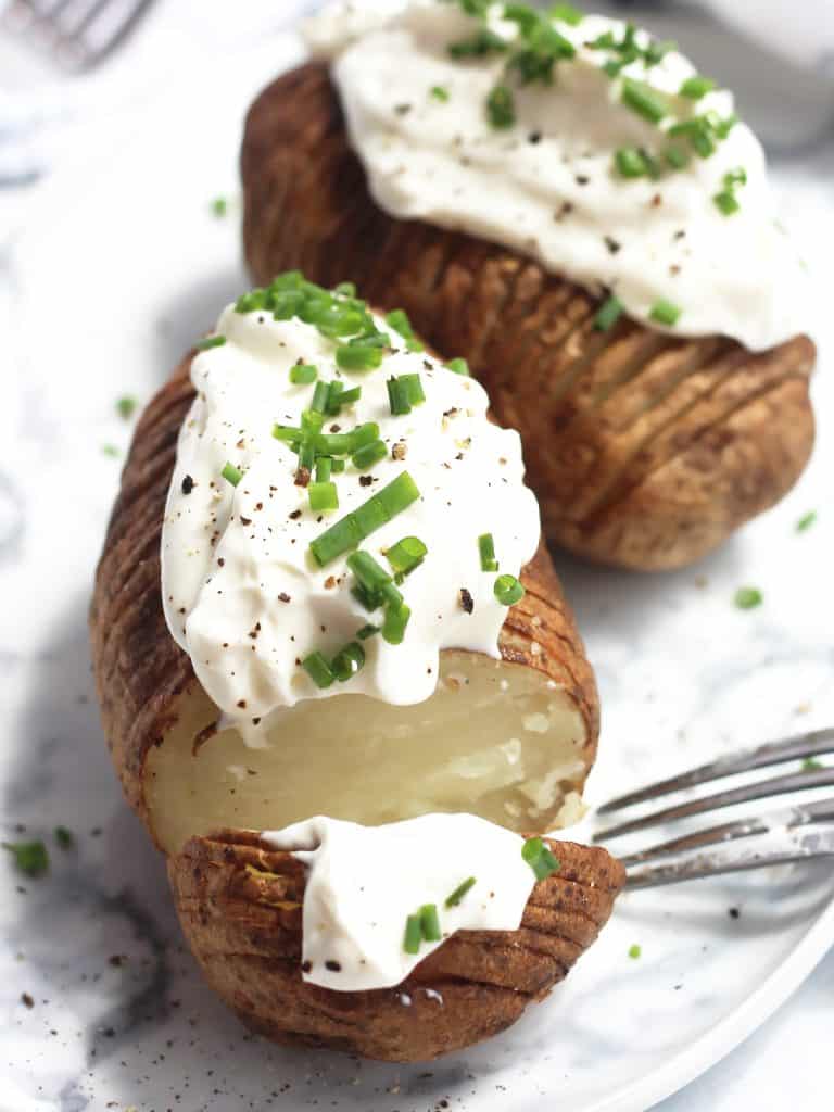 Two hasselback potatoes on a plate with a fork, one sliced open.