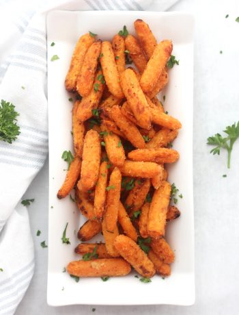 Air fryer carrots on a white serving plate next to a blue and white cloth with parsley garnish.