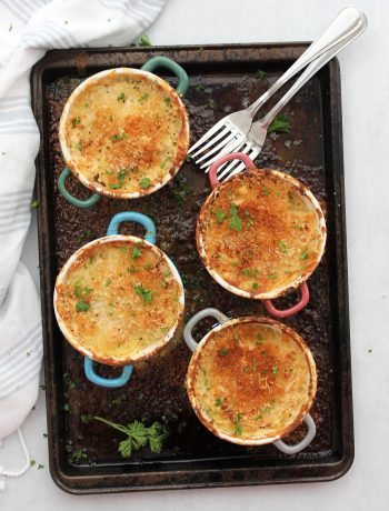 Four individual potato gratins on a baking sheet and garnished with fresh herbs.