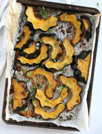 Maple roasted acorn squash on a parchment lined baking sheet.