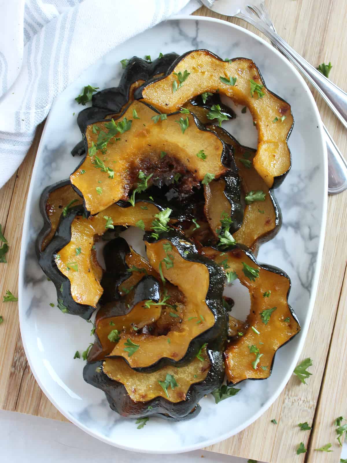 Overhead shot of maple roasted acorn squash on a serving plate next to two forks.