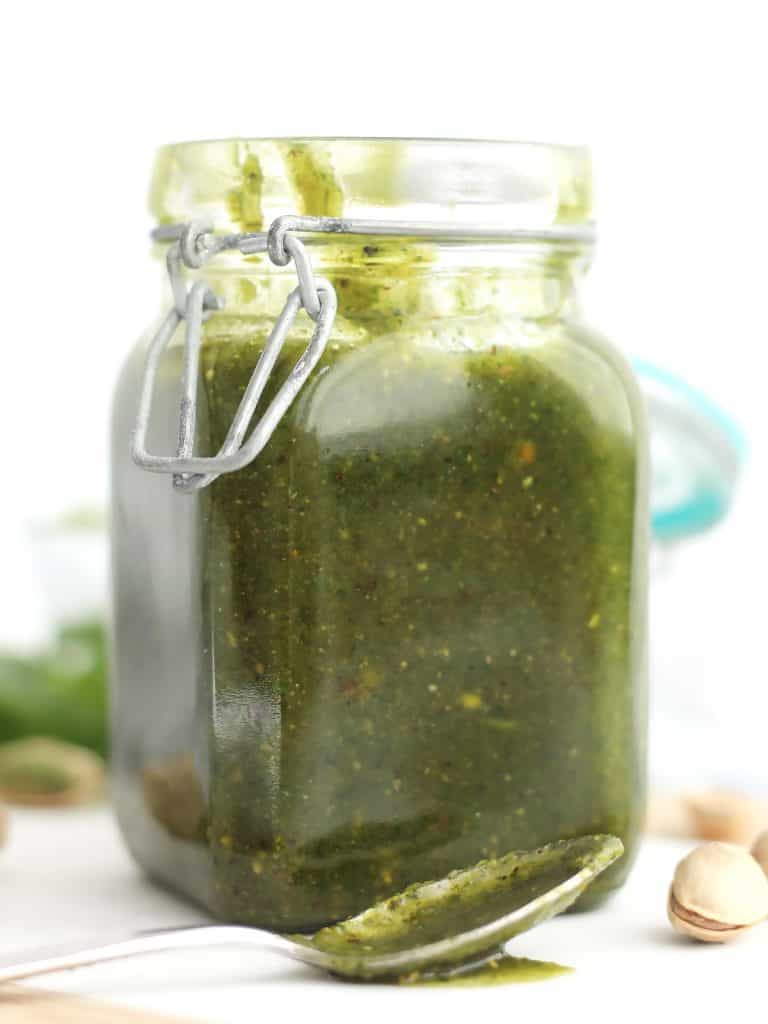 A jar of green pesto next to a spoon.