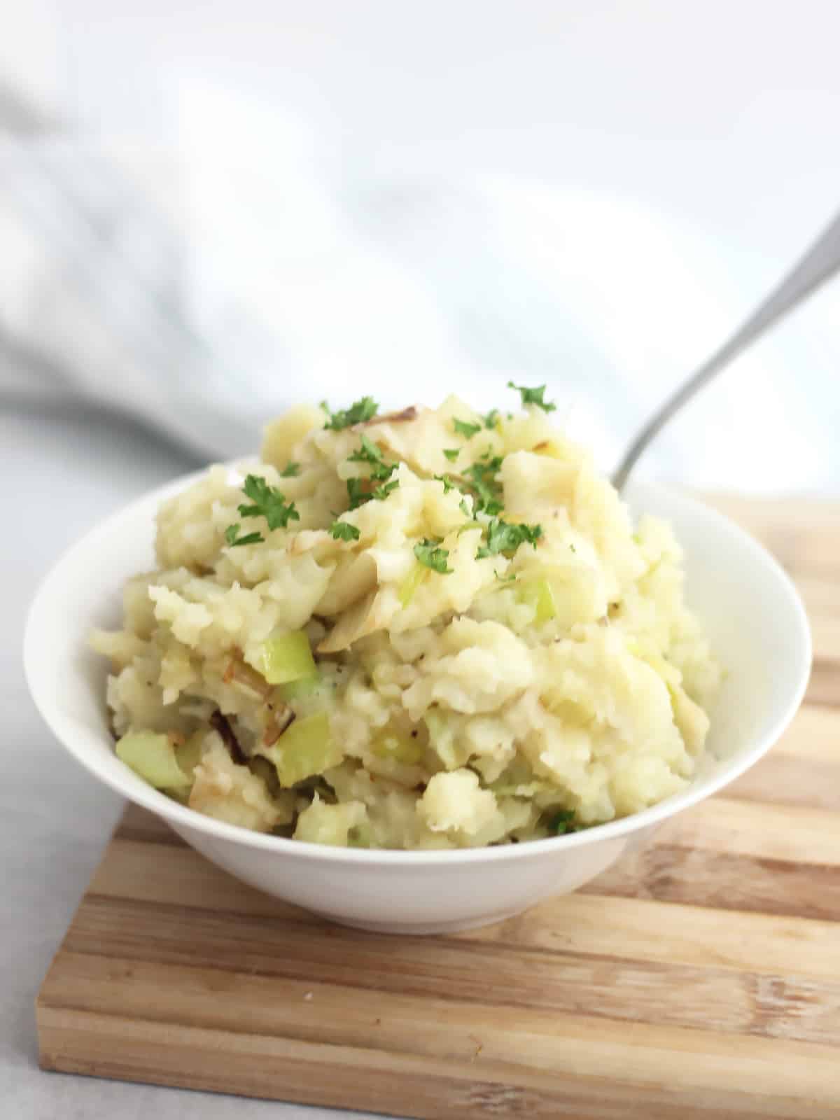 A spoon in a bowl of mashed potatoes with sautéed leeks.