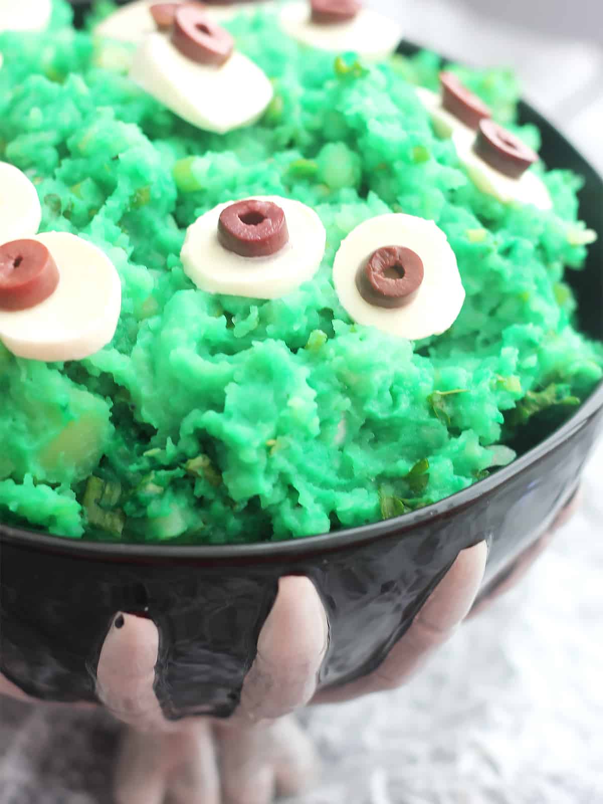 Green mashed potato with eyes in a black bowl.