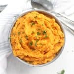 Whipped sweet potatoes in a blue bowl with fresh parsley garnish.