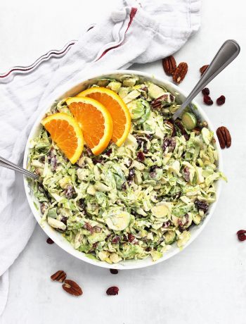 Brussels sprout slaw with pecans and cranberries in a bowl topped with orange slices.