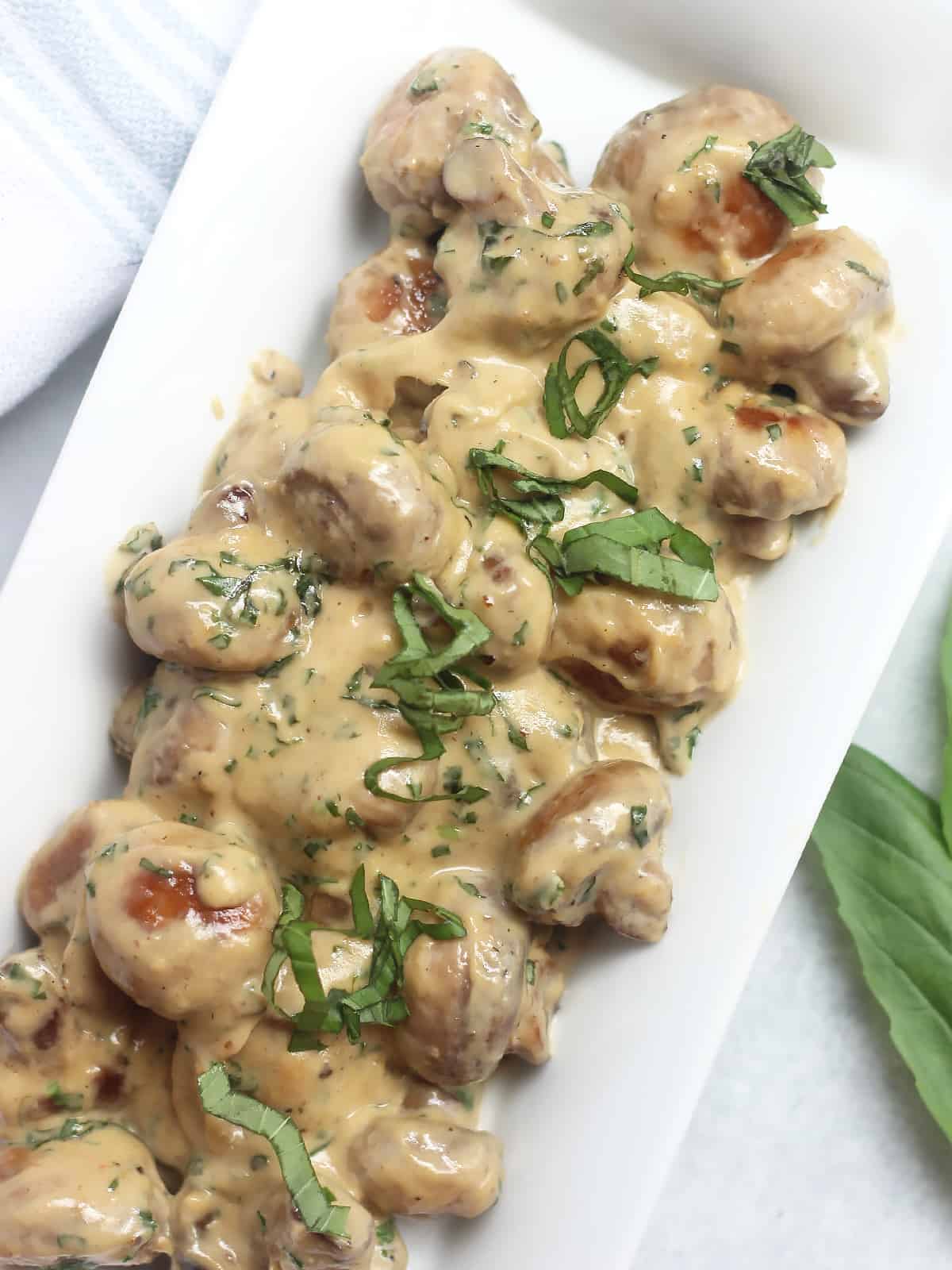 Overhead shot of creamy basil mushrooms on a white serving plate.