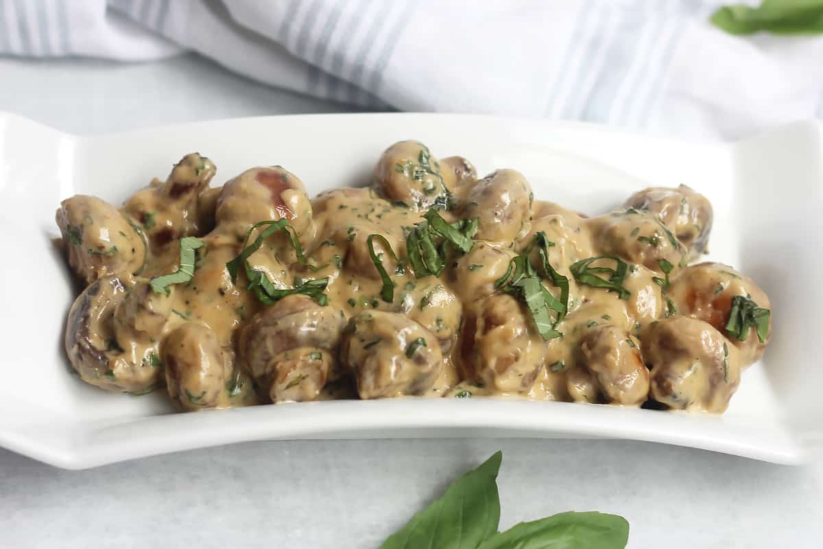 Creamy basil mushrooms on a white serving plate.
