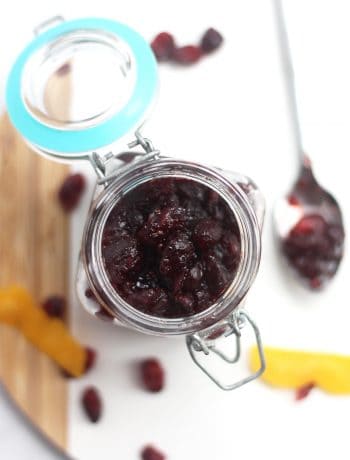 Cranberry sauce in a glass jar on a cutting board.